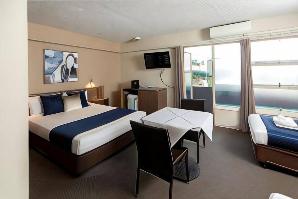 Quarto de hotel com cama, escrivaninha, cadeira, televisão e janela com vista.