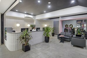 A reception area with a curved counter, potted plants, a receptionist, and a seating area with a sofa and a small table. - The Metropolitan Spring Hill (Spring Hill)