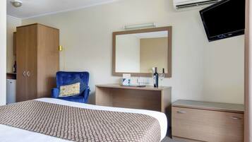 Hotelkamer met een bed, bureau, stoel, kledingkast, spiegel, flatscreen-tv en airconditioning.