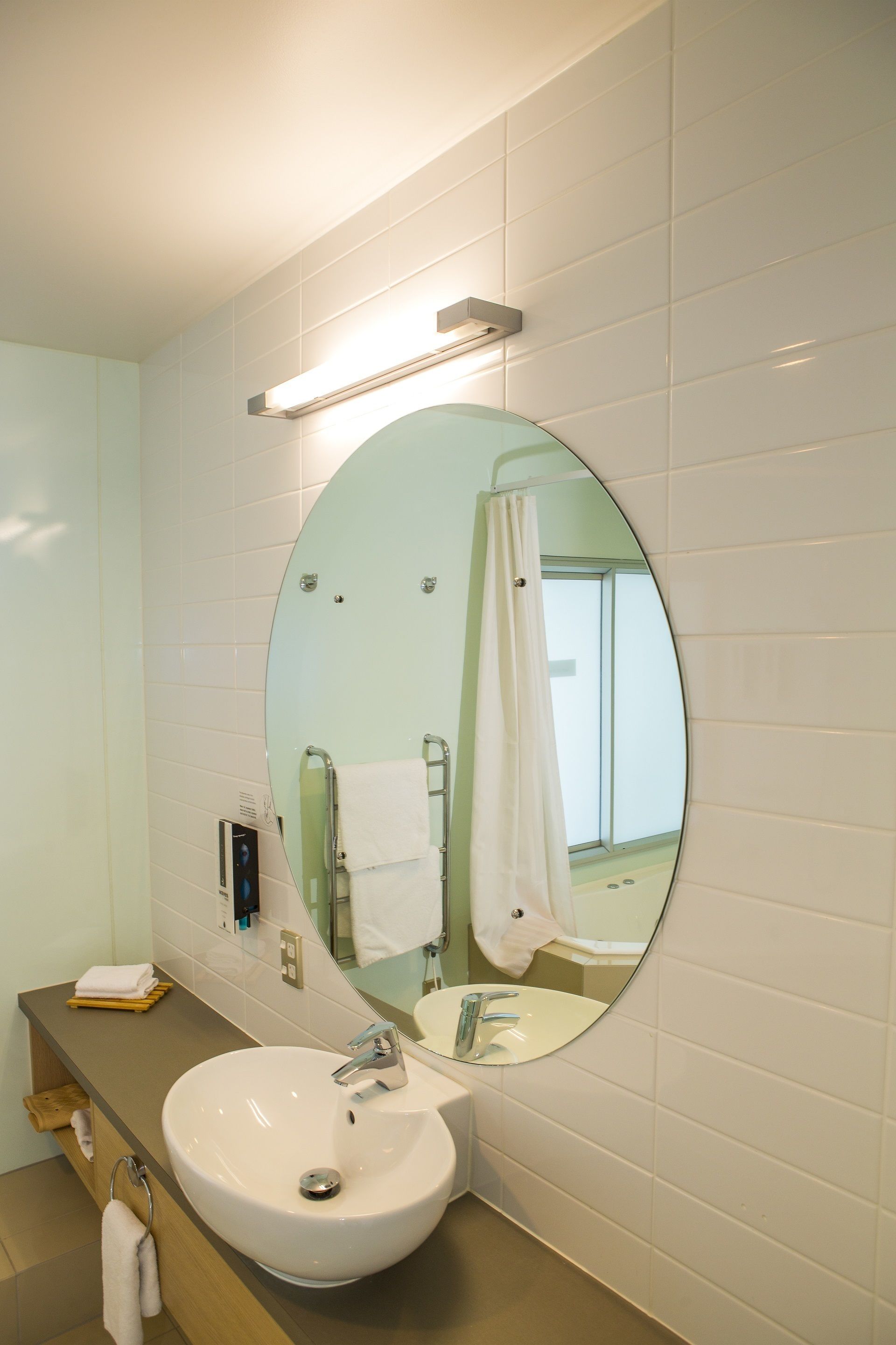 A bathroom with a round mirror, white sink, and a towel rack.