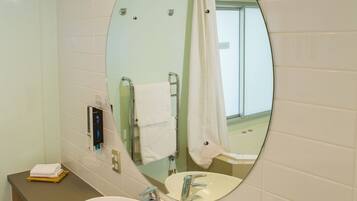 A bathroom with a round mirror, white sink, and a towel rack.