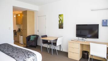 Een moderne hotelkamer met een bed, een bureau met een televisie, een stoel, een kleine kitchenette en een prullenbak.