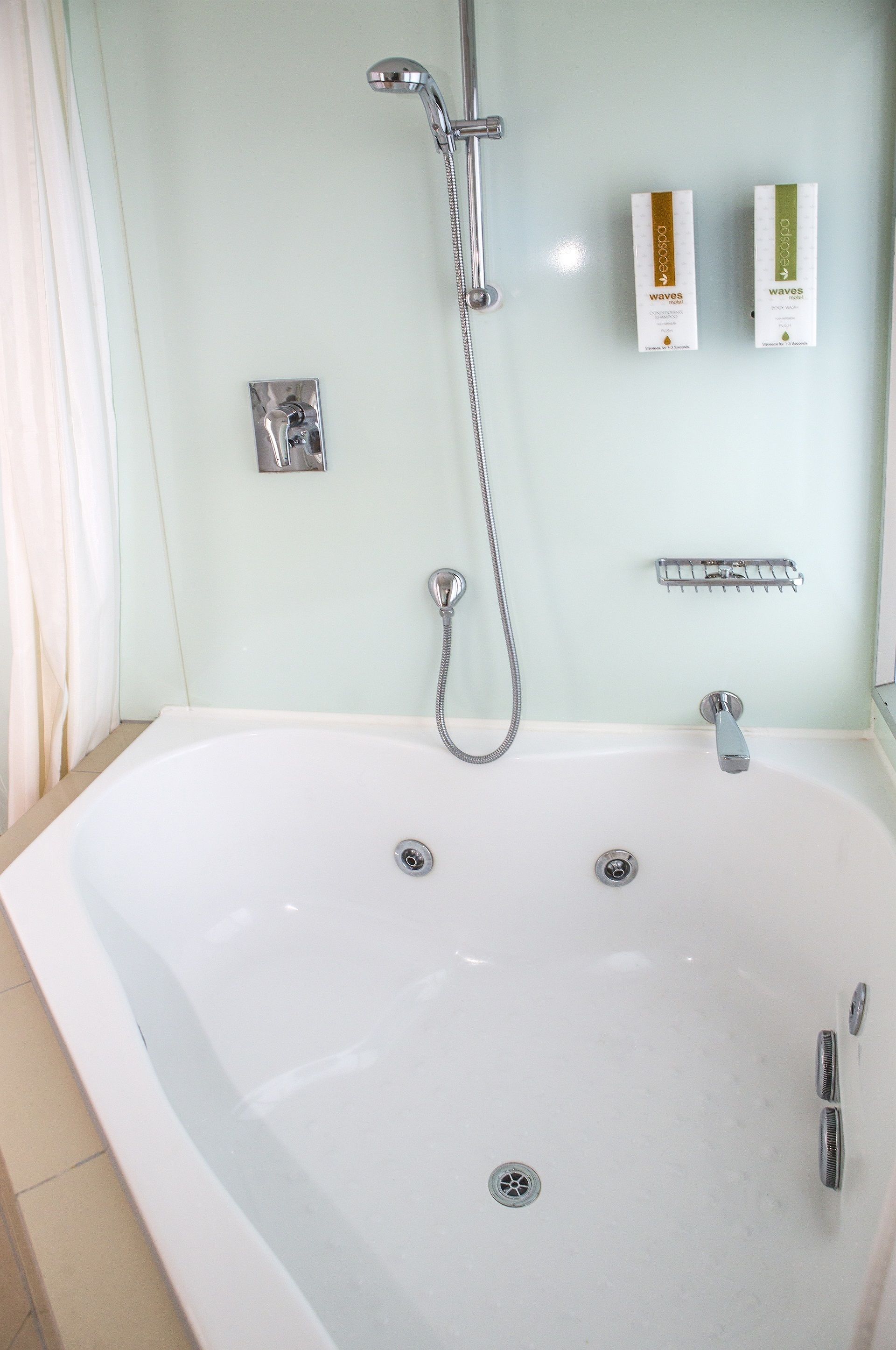 A bathroom with a large bathtub, a showerhead, and two toiletries on the wall.