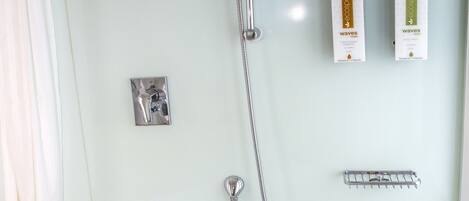 A bathroom with a large bathtub, a showerhead, and two toiletries on the wall.