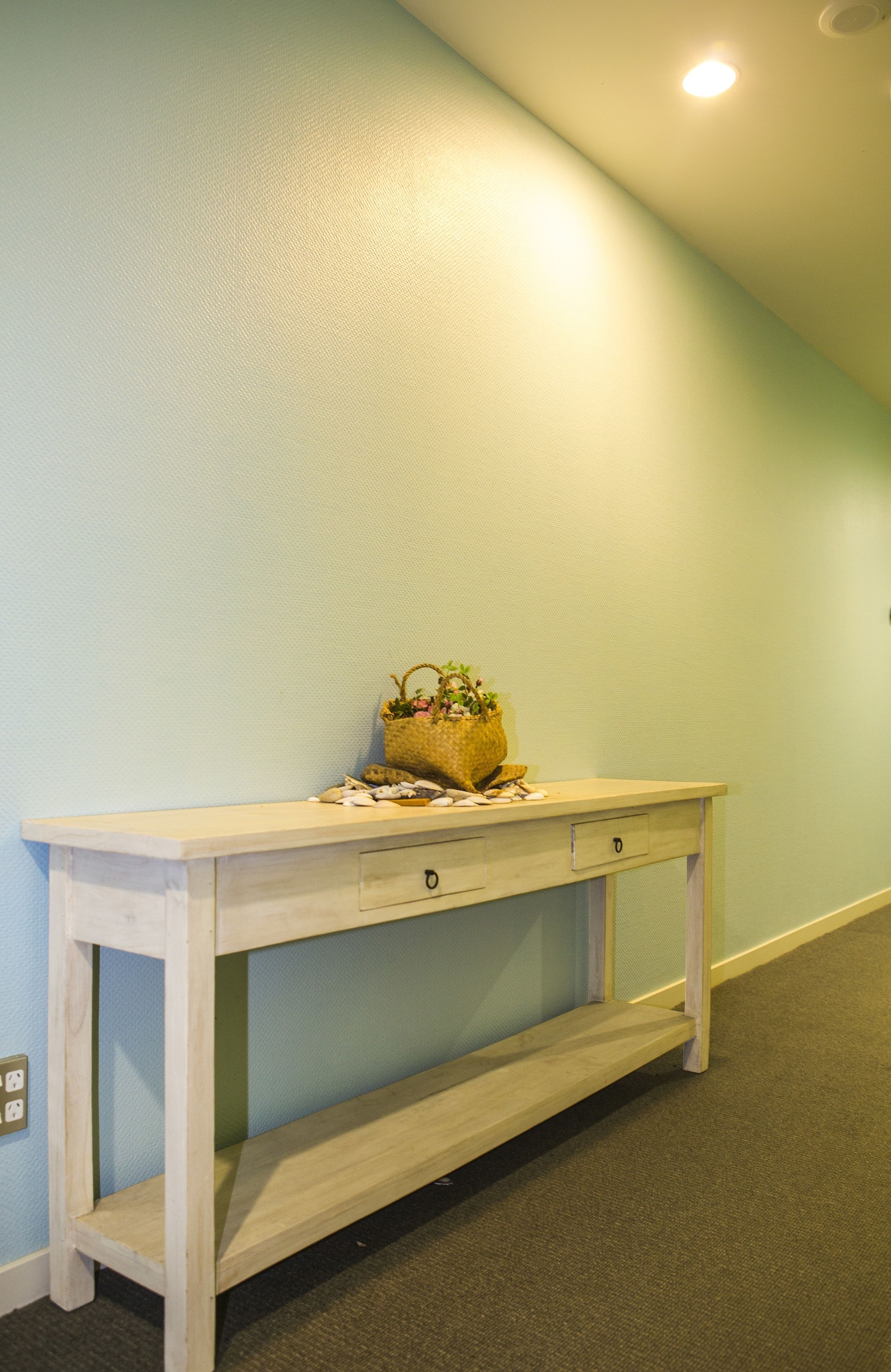 A wooden console table with a basket of flowers and a small plant, against a light blue wall.