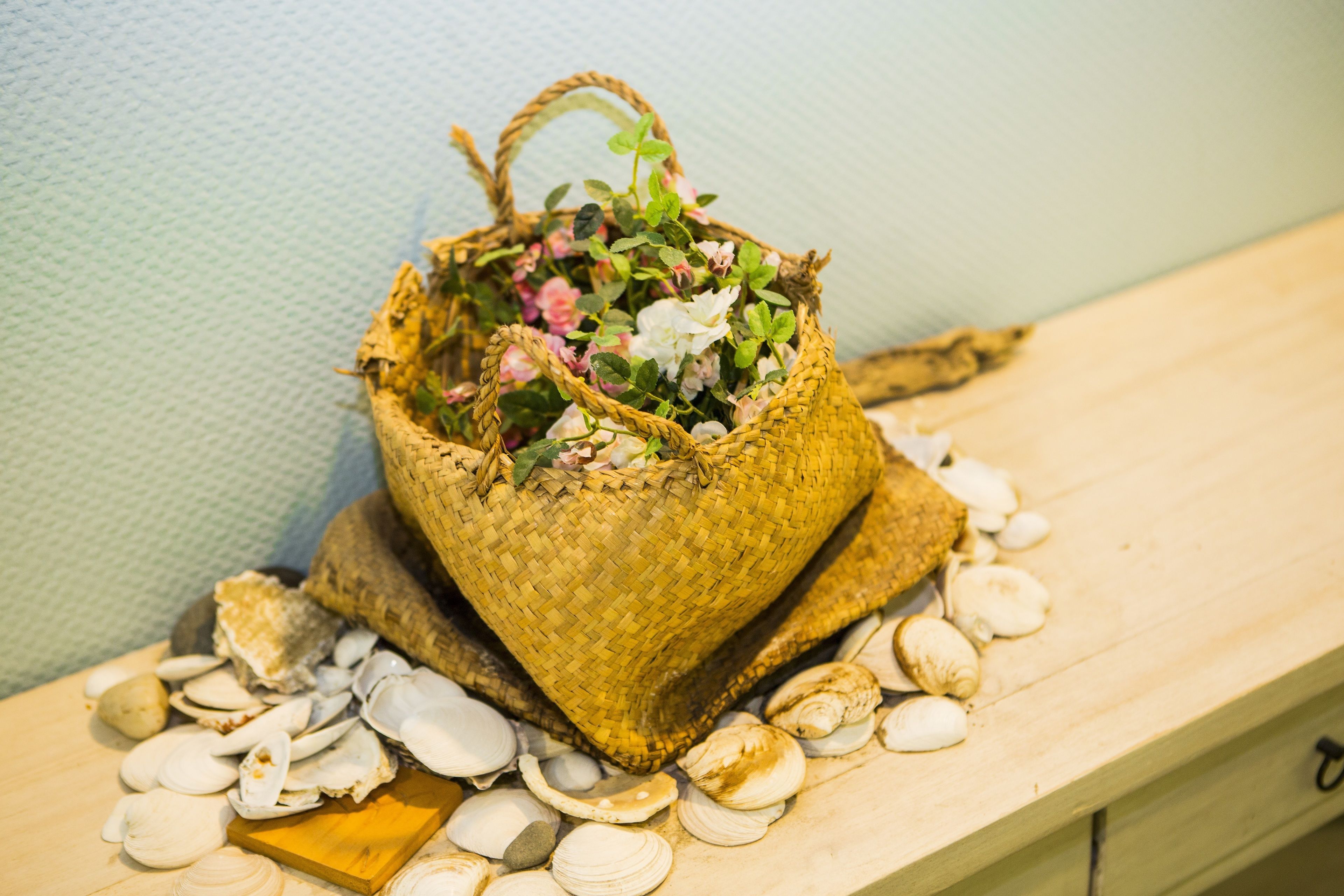 Een gevlochten mandje gevuld met bloemen en schelpen op een houten ondergrond.