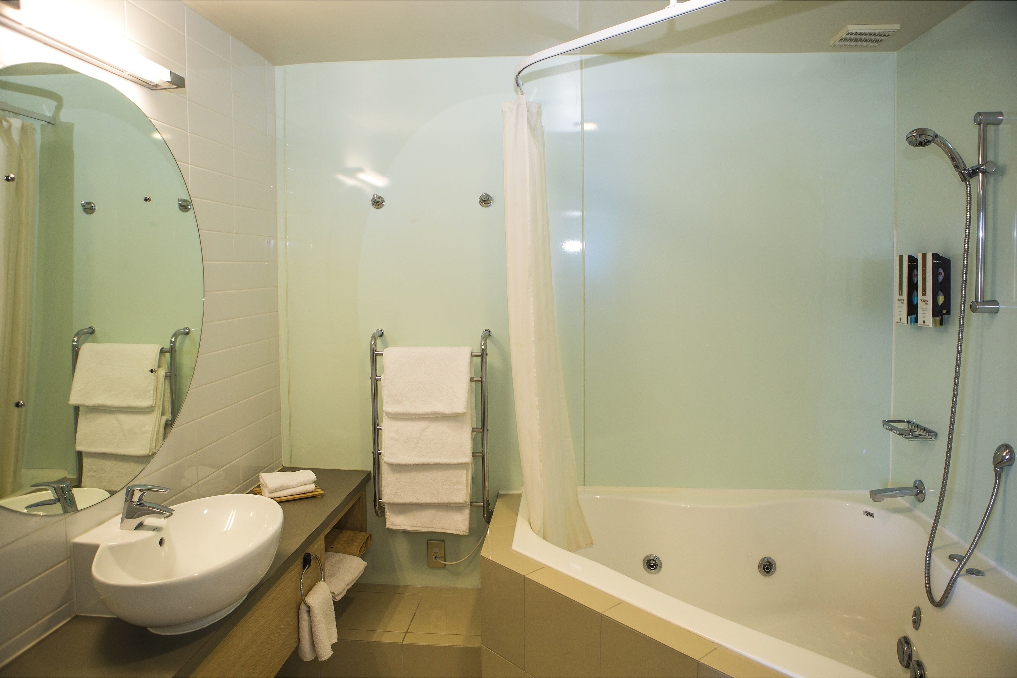 Un baño con lavamanos, espejo, toallero y cabina de ducha con mampara de vidrio.