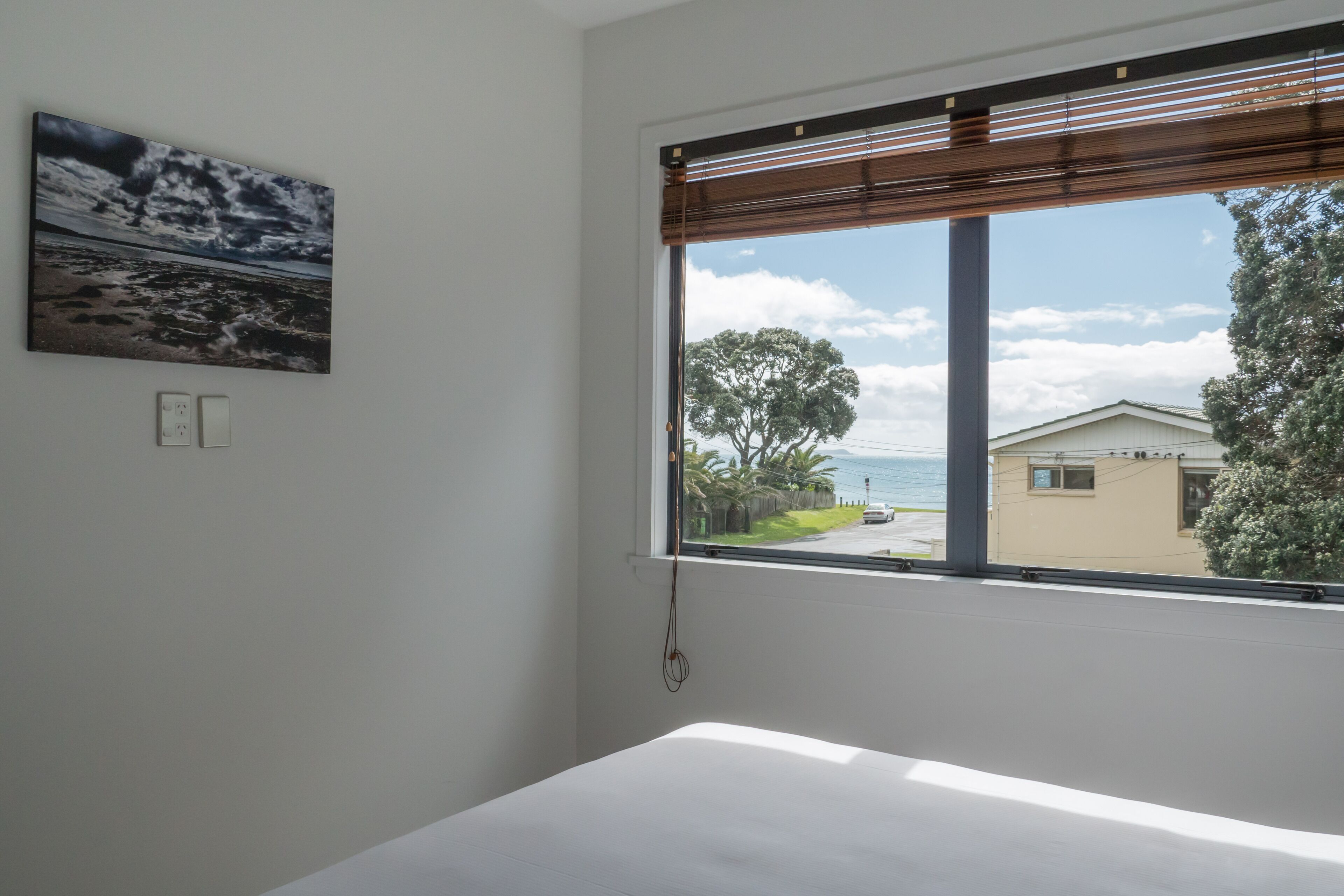 A room with a large window offering a view of a beach and a house.