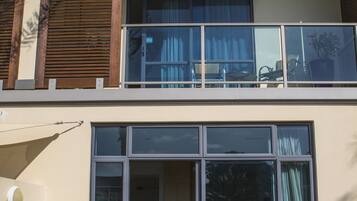 Un edificio de dos pisos con un balcón, grandes puertas correderas de vidrio y una mesa redonda de madera con cuatro sillas.
