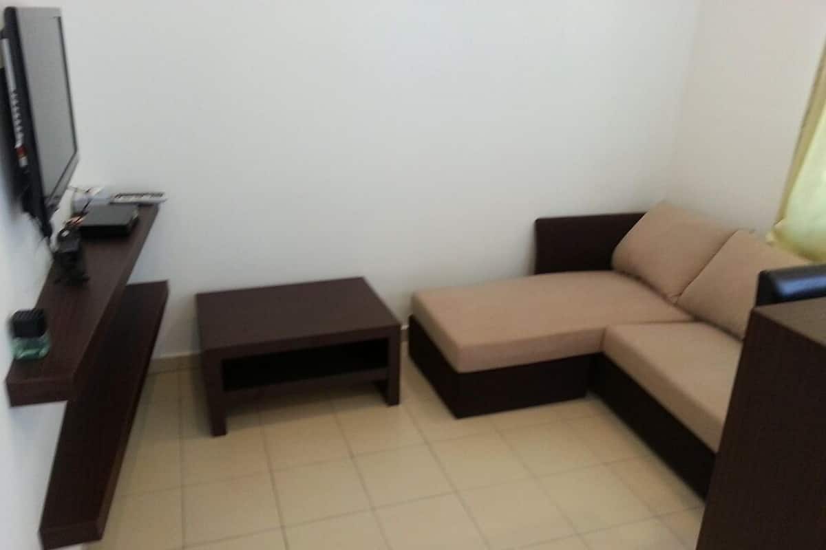 Una sala de estar con un sofá marrón, una mesita y un televisor sobre un mueble.