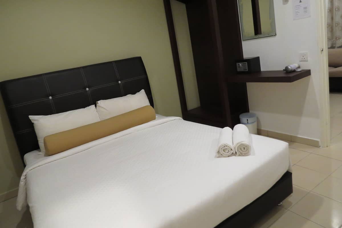 Una cama bien hecha con un cabecero negro, almohadas blancas y beige, y toallas enrolladas sobre la cama.