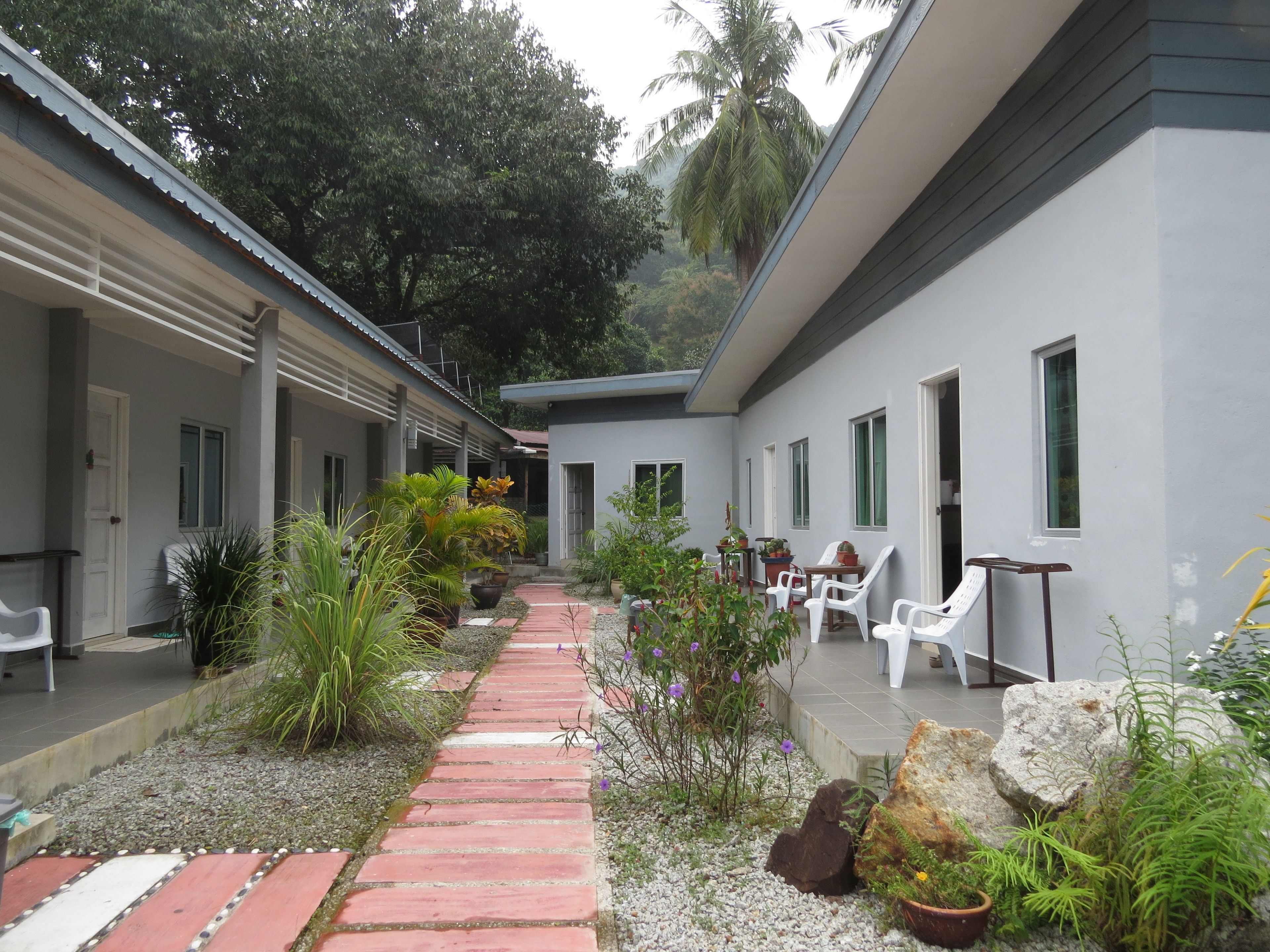 A corridor with potted plants, a brick pathway, and white furniture.