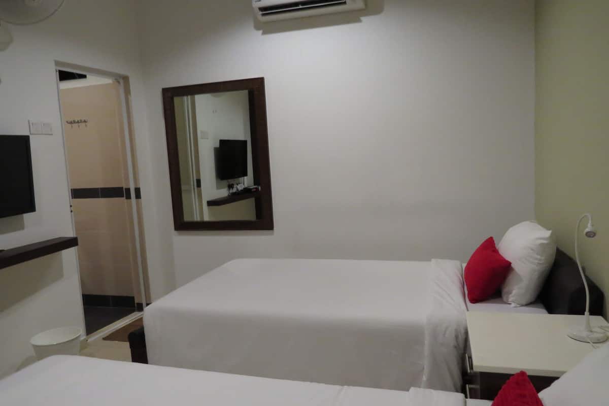 Habitación de hotel con dos camas, televisión, aire acondicionado, espejo y mesita de noche con lámpara.