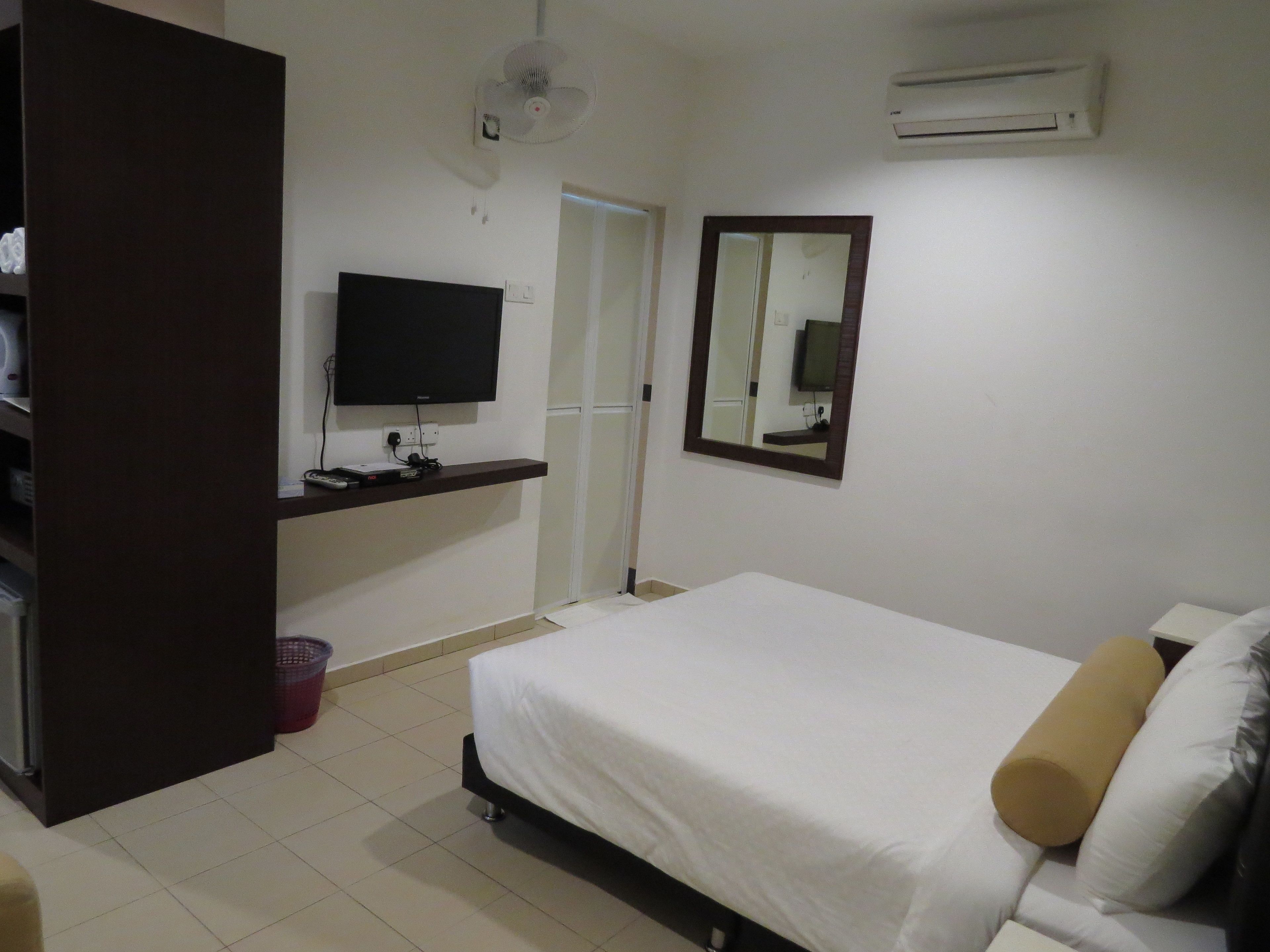 Un dormitorio con cama, televisión, espejo, aire acondicionado y armario.