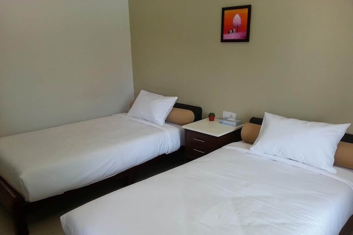 Una habitación de hotel con dos camas individuales, una mesita de noche pequeña con lámpara y un cuadro en la pared.