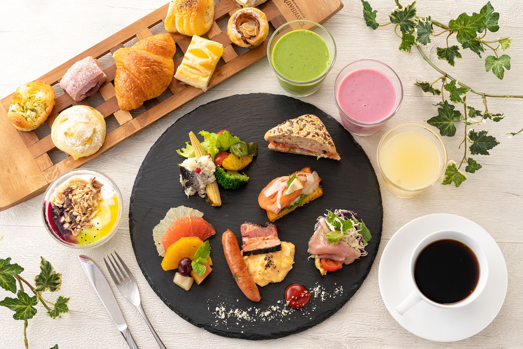 A variety of breakfast items on a black slate plate, including pastries, sandwiches, and fruit.