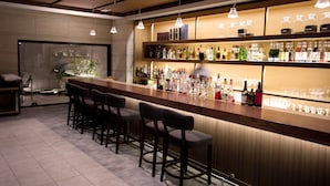 A bar area with a long counter, multiple stools, and shelves stocked with bottles and glasses. - Sakura Terrace (Kyoto)
