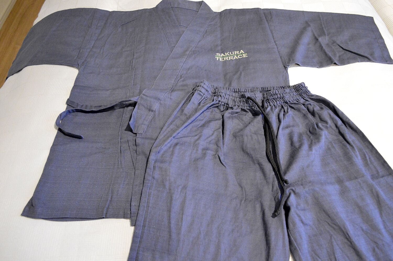 Una cama con un albornoz y pantalones grises dispuestos sobre ella.