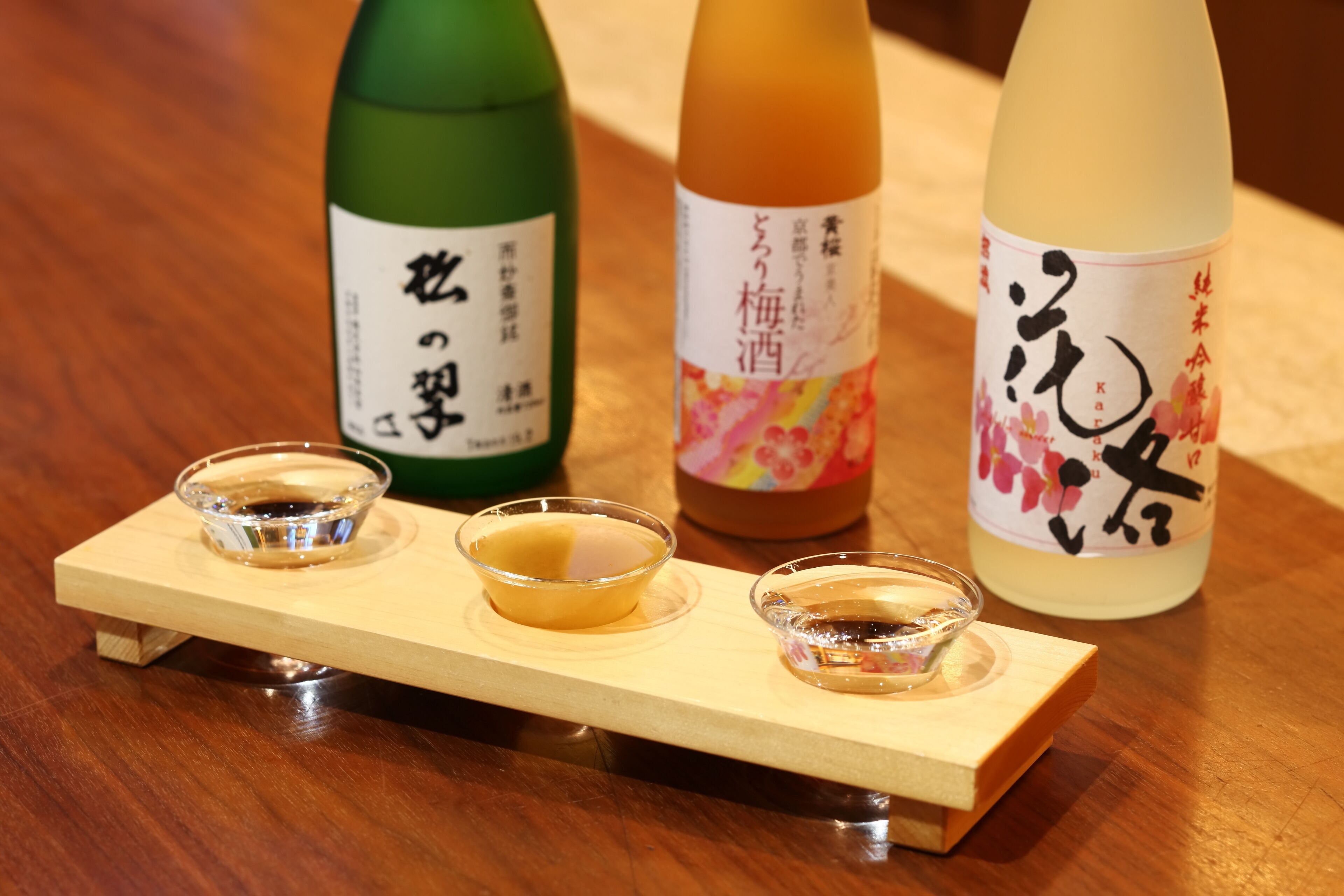 Tres botellas de sake sobre una bandeja de madera con dos pequeños cuencos de sake.