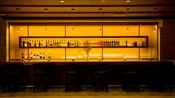 A bar area with multiple shelves of bottles and glasses, wooden bar stools, and hanging lights.