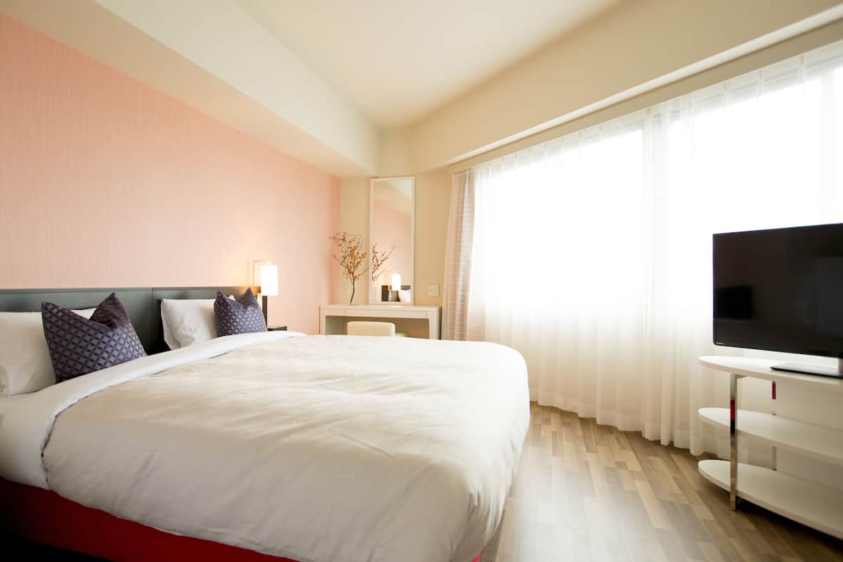 A hotel room with a large bed, a TV, a desk, and a window with curtains.