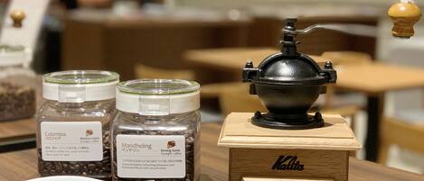 Two coffee jars labeled "Colombia" and "Mandheling" on a wooden table with a coffee grinder.