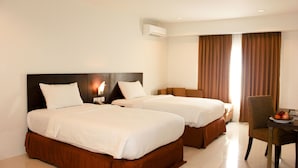 A hotel room with two beds, a desk with a chair, and a dining table with fruit. - Grand Asia Hotel (Makassar)