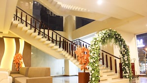 A modern hotel lobby with a staircase, a reception desk, and a floral archway. - Grand Asia Hotel (Makassar)
