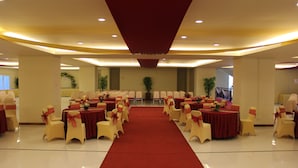 A banquet hall with a red carpet aisle, round tables, and chairs with red sashes. - Grand Asia Hotel (Makassar)