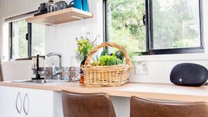 Een moderne keuken met witte kastjes, een houten aanrecht, twee bruine barkrukken, een raam met uitzicht op groen en een plank met potten en bakjes.