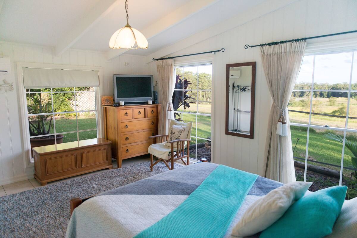 Une chambre avec un grand lit, une commode en bois, une télévision et une vue sur l’extérieur.