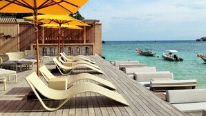 A wooden deck with lounge chairs and yellow umbrellas, overlooking turquoise waters with boats. - Beach Club by Haad Tien (Koh Tao)