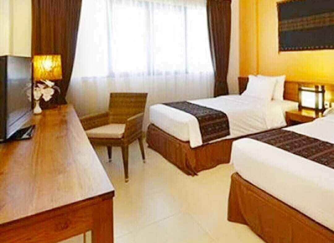 A hotel room with two beds, a desk, a chair, and a TV.