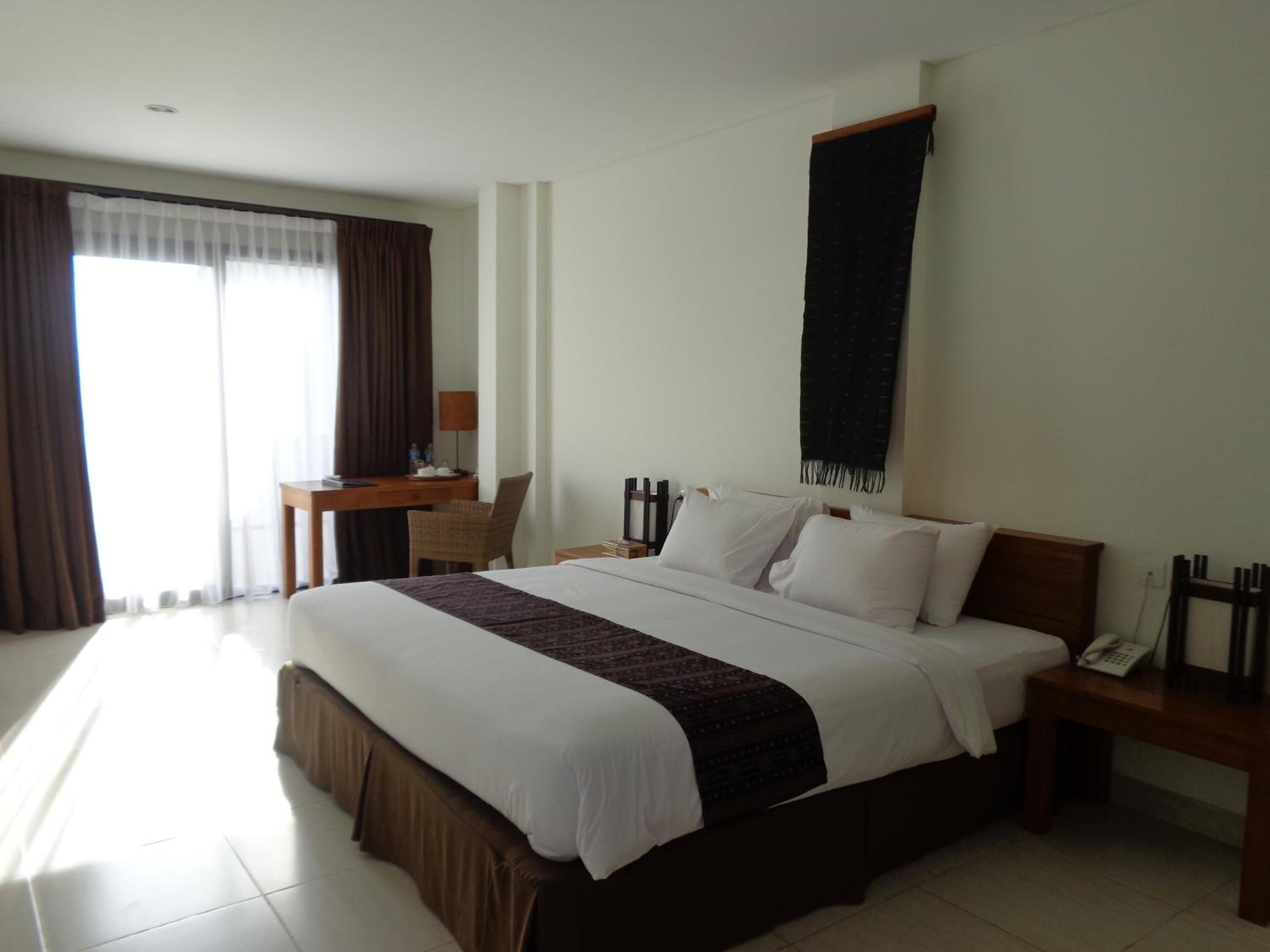 A hotel room with a large bed, a desk, a chair, a phone, and a window with curtains.