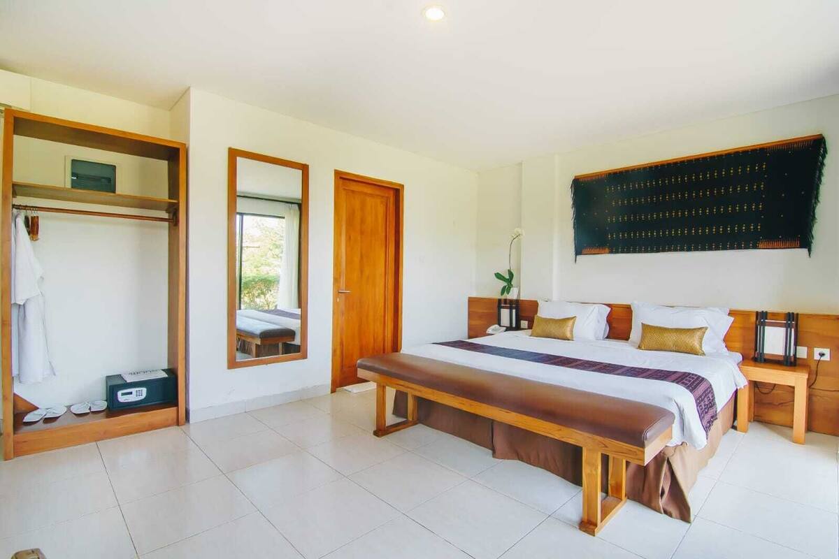 Ein Schlafzimmer mit einem großen Bett, einer hölzernen Bank, einem Kleiderschrank und einem Spiegel.