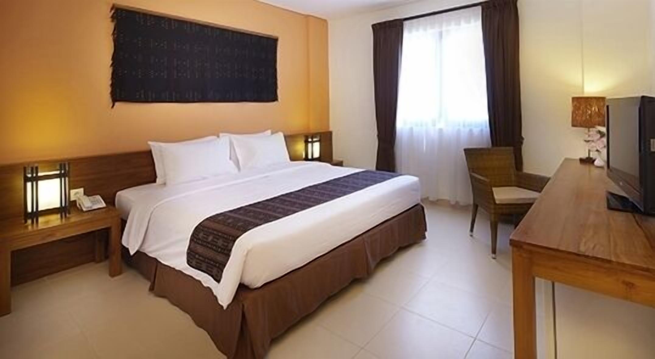A hotel room with a large bed, a desk with a television, and a chair.