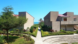 Un chemin mène à un bâtiment surmonté d’un toit rouge, entouré d’une végétation bien entretenue et offrant une vue dégagée sur la mer.