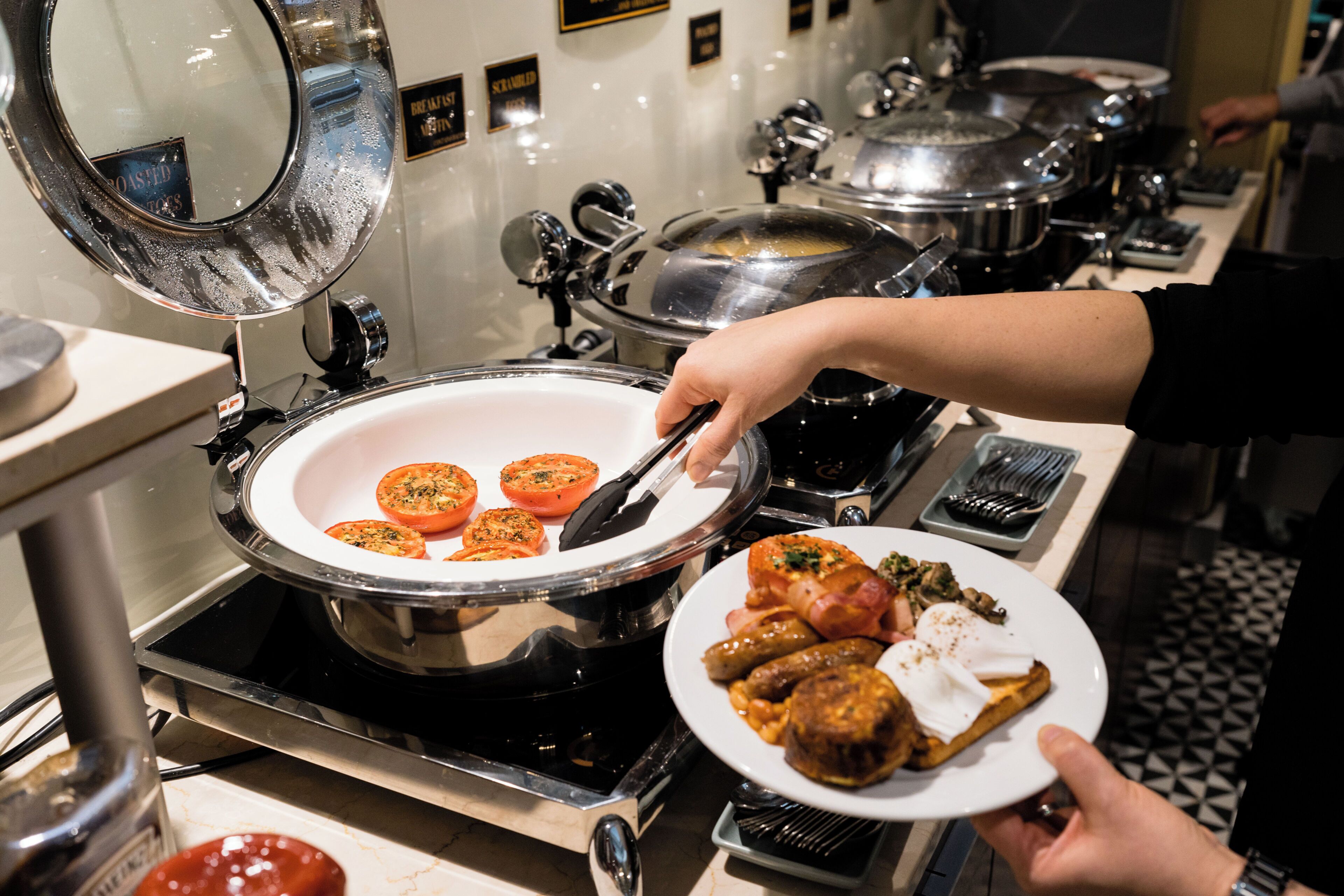 A buffet setup with a hot plate, serving utensils, and a plate with food.