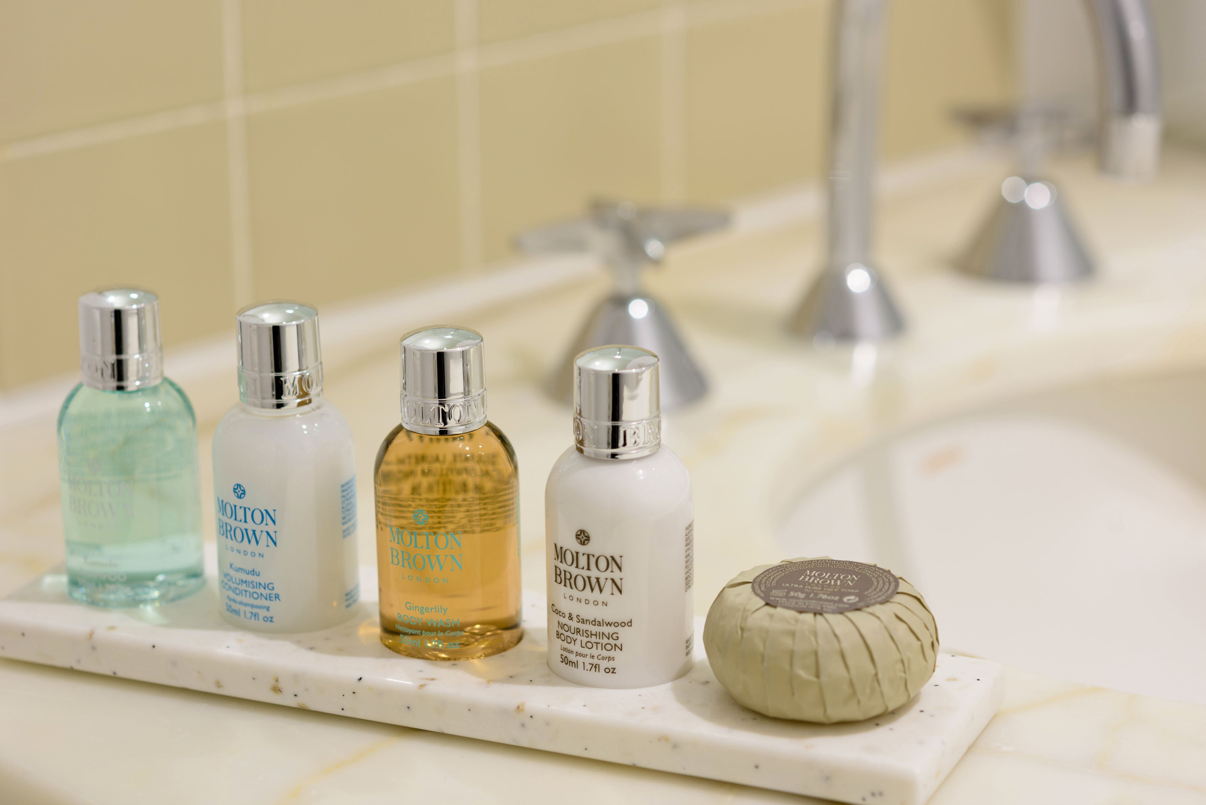 A bathroom shelf with four bottles of Molton Brown body lotion and one bar of soap.