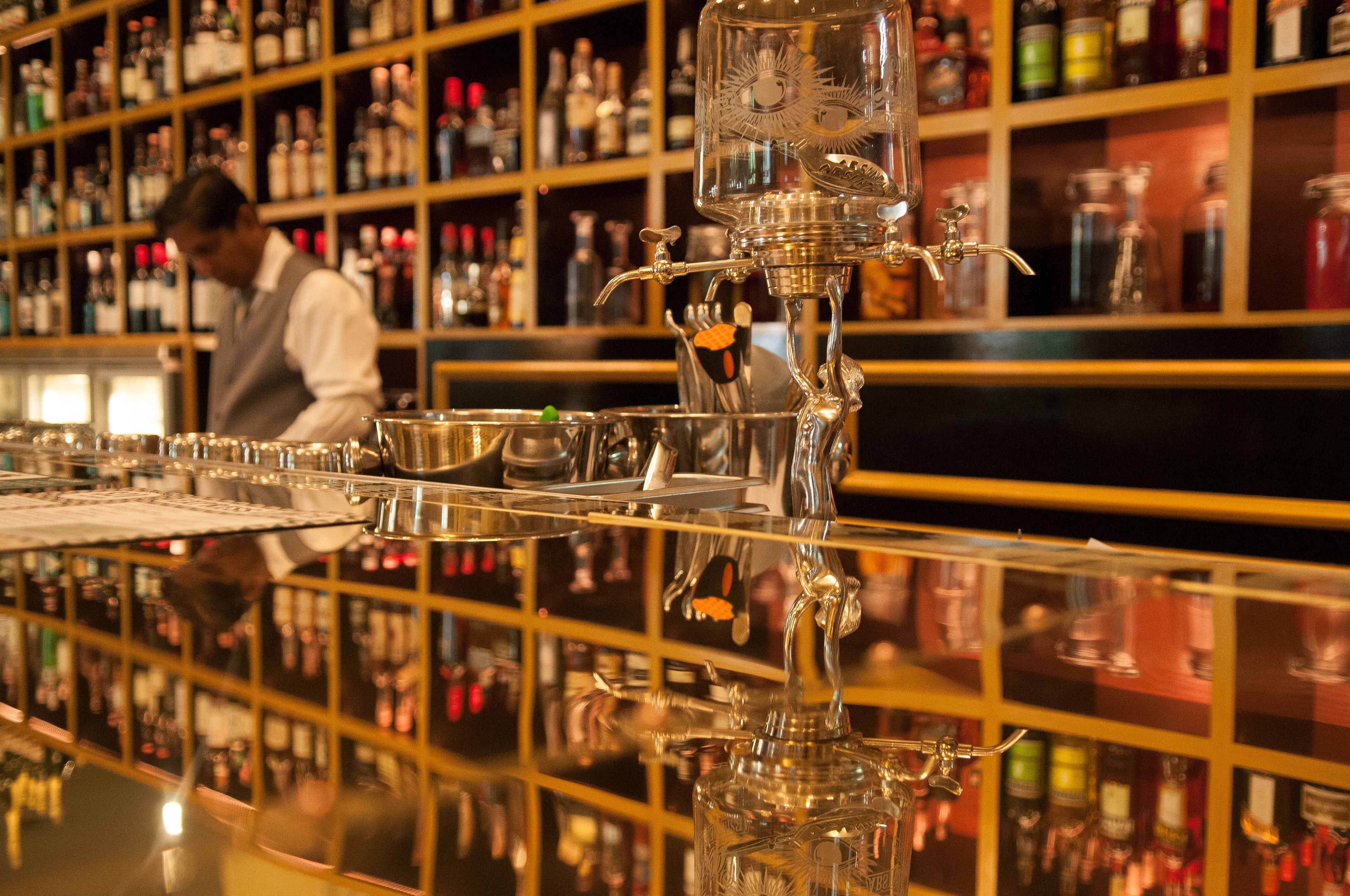 Un bar con una barra pulida y un cantinero preparando bebidas.