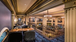 Un amplio vestíbulo de hotel con detalles ornamentales en oro, una escalera central y varias salas de comedor.