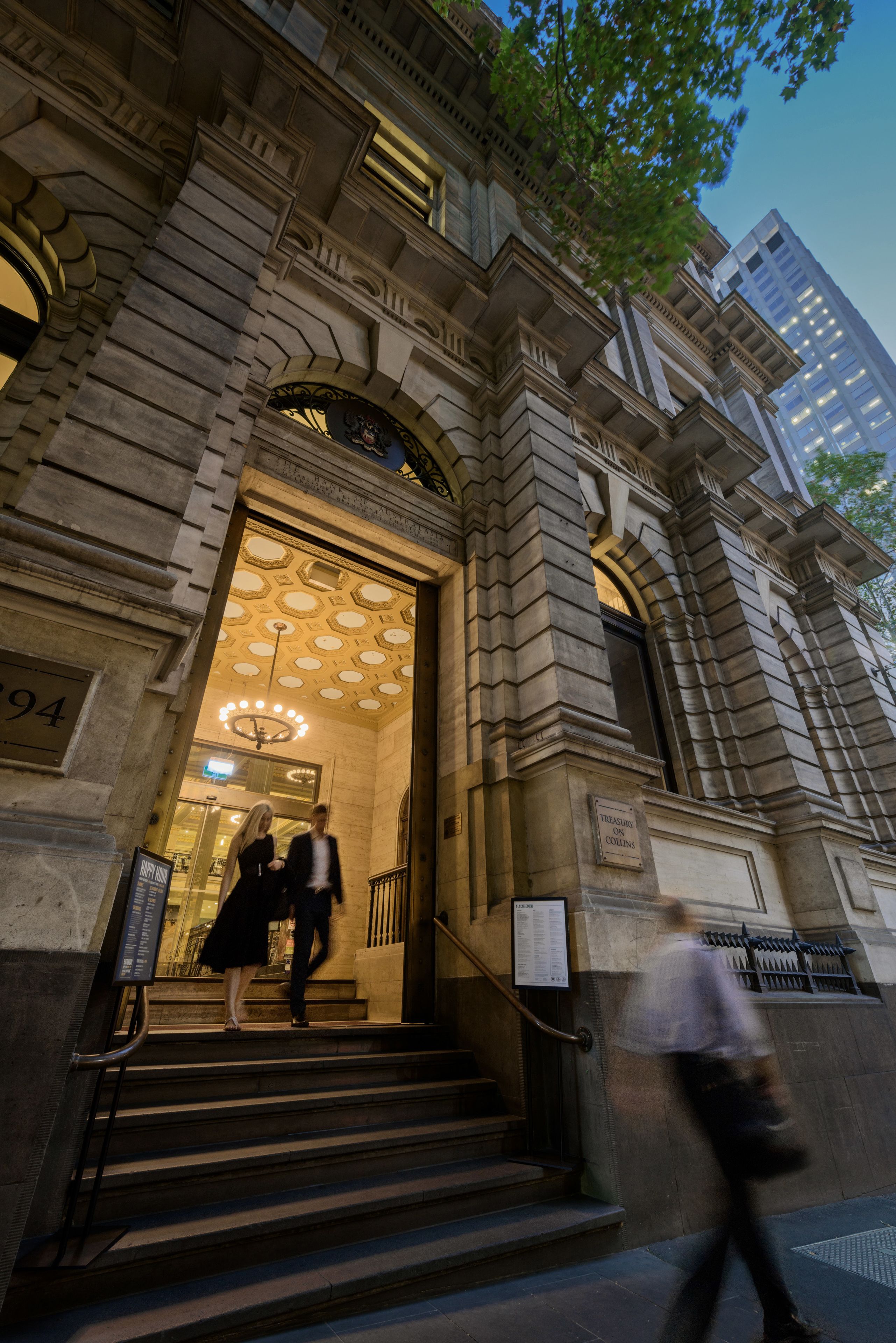 A grand building entrance with a large arched doorway, a staircase leading up, and a sign reading "Treasury on Collins."