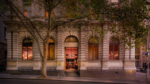 Un edificio histórico con ventanas arqueadas y una entrada imponente, con un árbol en primer plano.