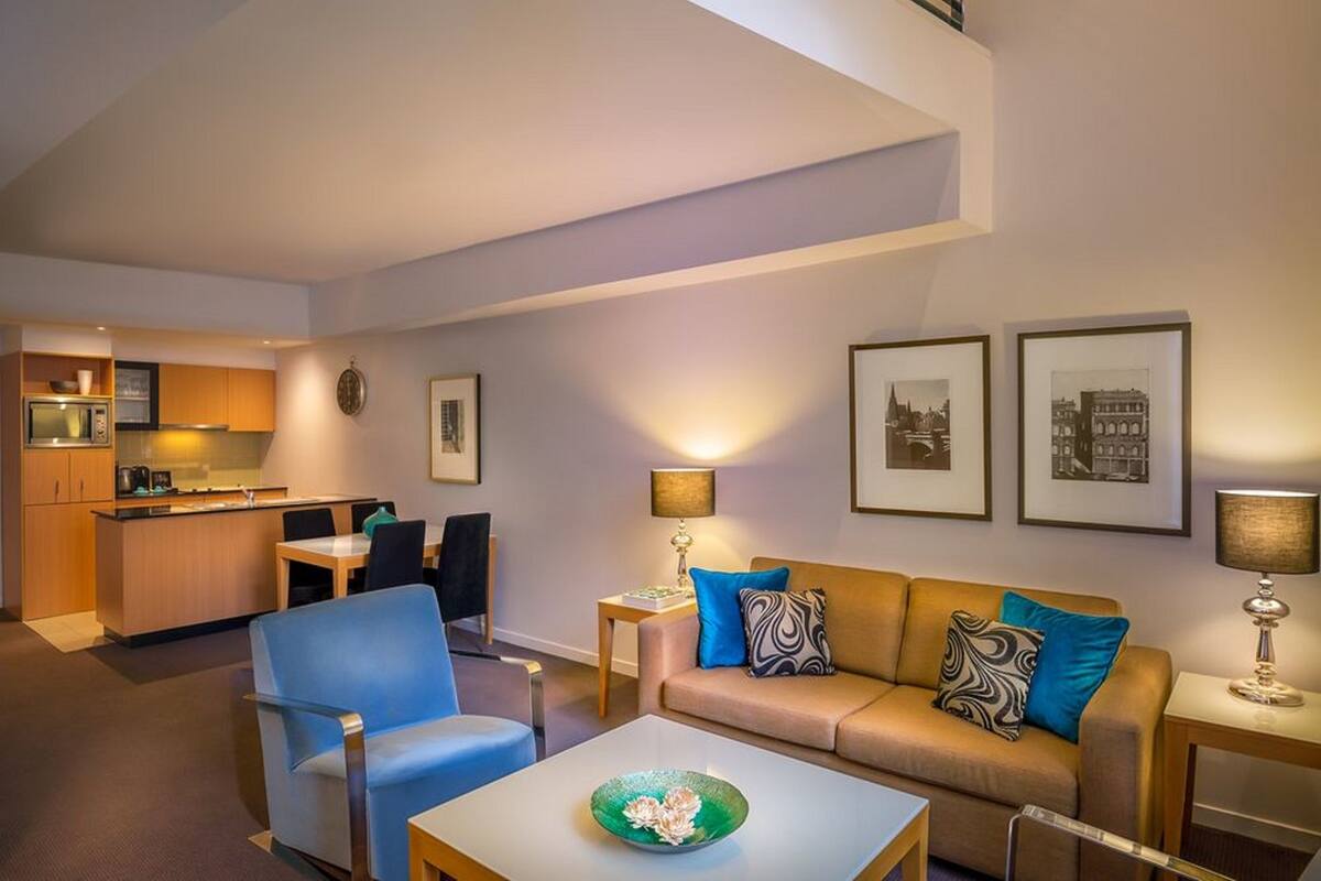 Uma sala de estar moderna com sofá, cadeiras, mesa de centro e cozinha ao fundo.