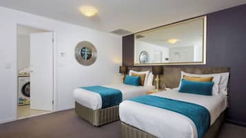 Une chambre d’hôtel avec deux lits, un grand miroir, une horloge ronde et un espace buanderie visible à travers une porte ouverte.