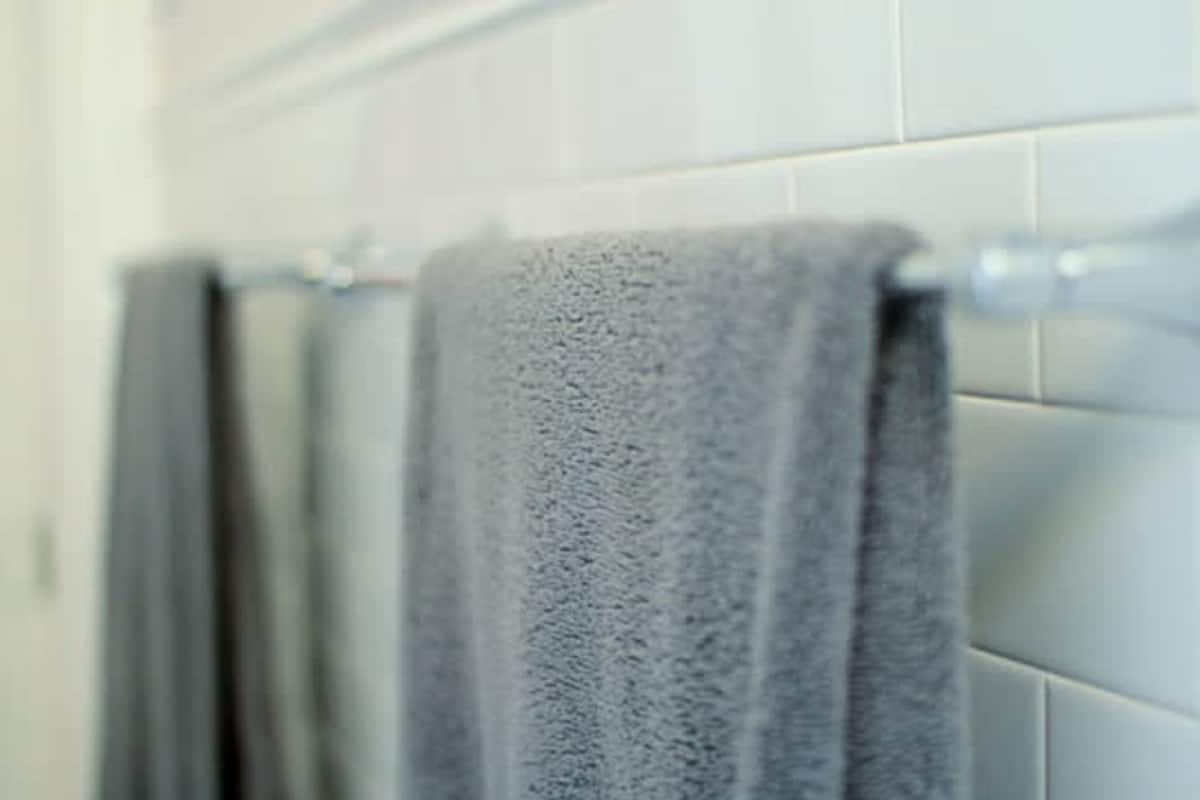 A bathroom with white tiled walls and a towel rack with two towels.