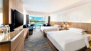 Une chambre d’hôtel dotée d’une grande télévision à écran plat, de deux lits, d’un bureau avec une machine à café et offrant une vue sur la piscine et la verdure.