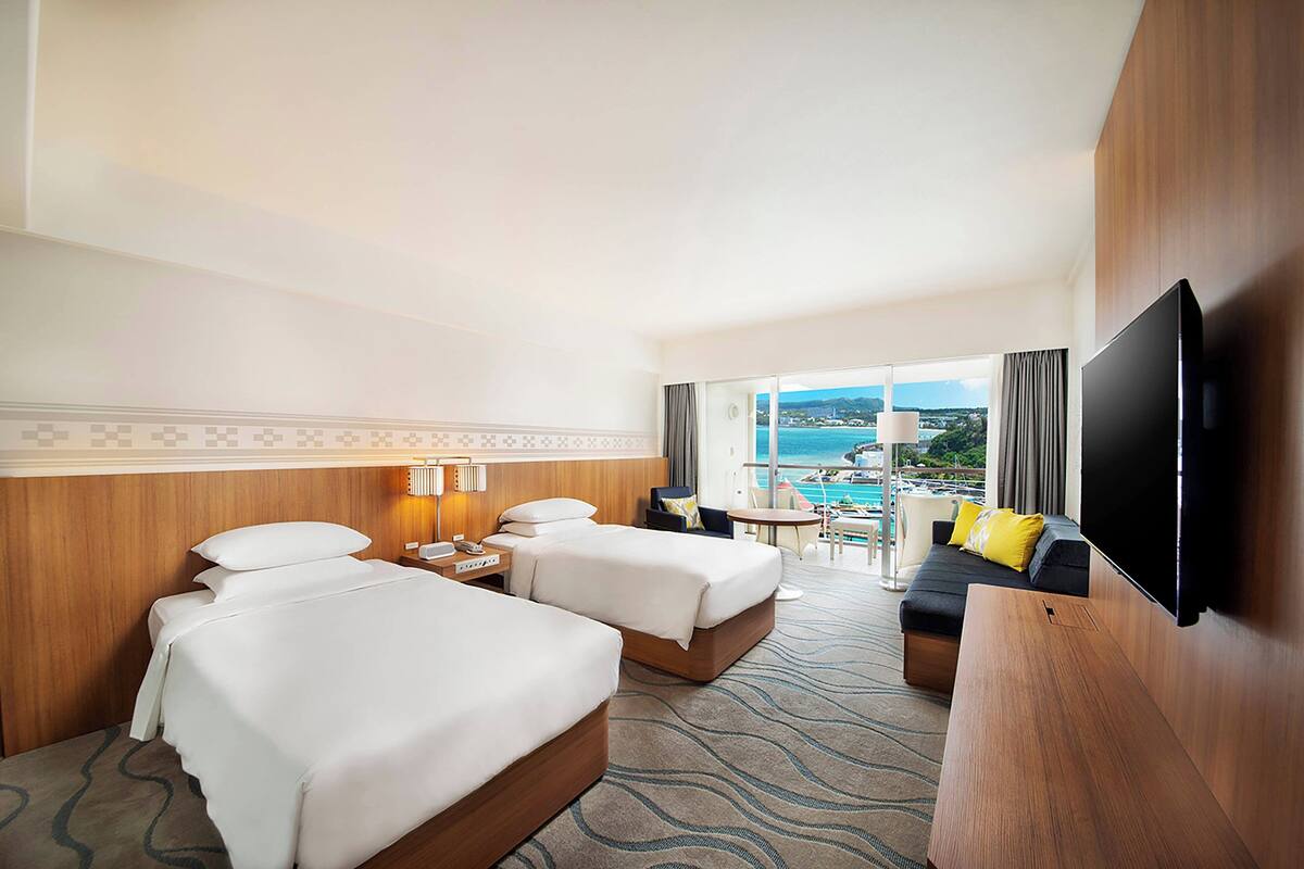 Una habitación de hotel con dos camas, televisión, escritorio y vista al océano.