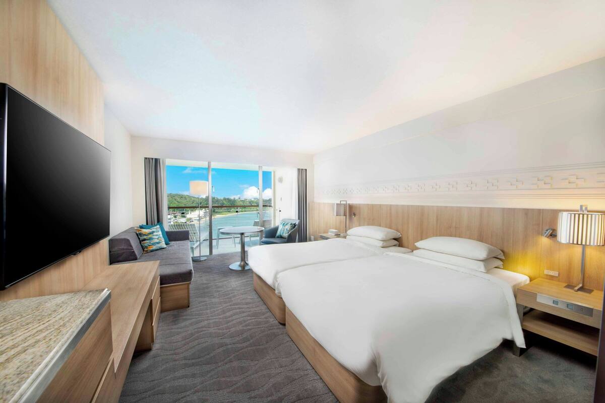 Habitación de hotel con una cama grande, un televisor de pantalla plana, un sofá, una mesita y vistas al exterior.