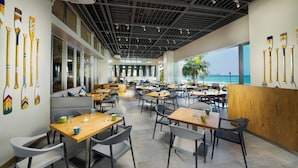 Une salle à manger spacieuse avec de hauts plafonds, un éclairage moderne et une vue sur l’océan.